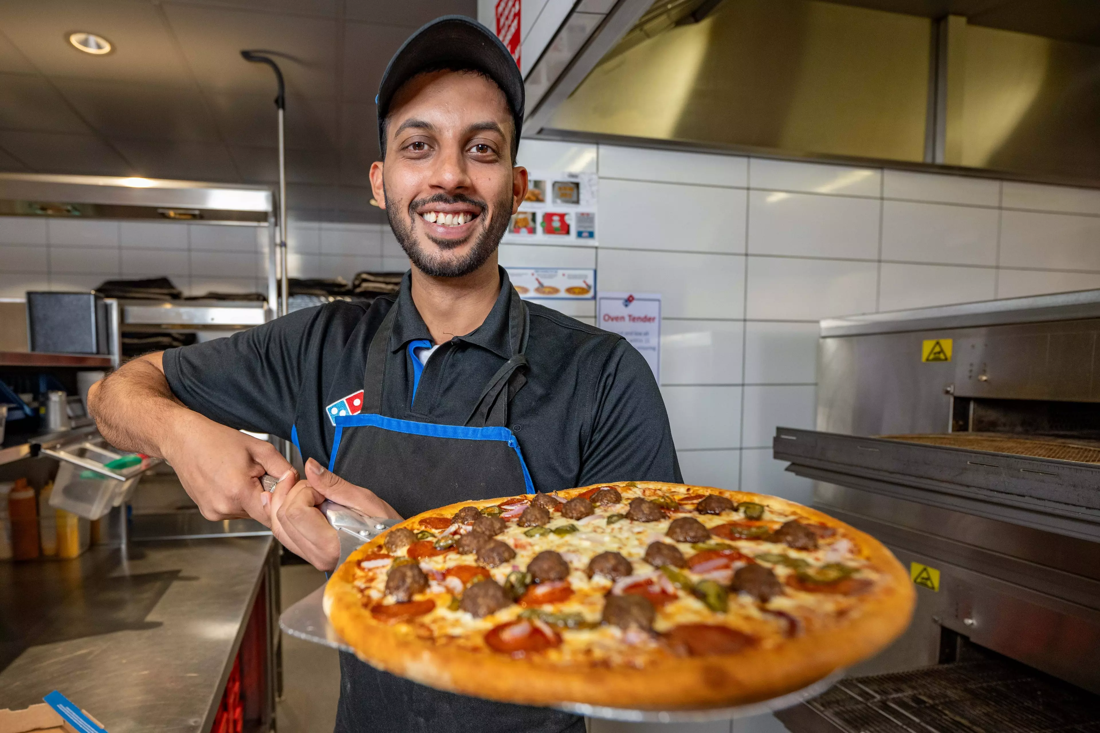 A Domino's Worker is standing in store holding a pizza on top of a pizza peel.