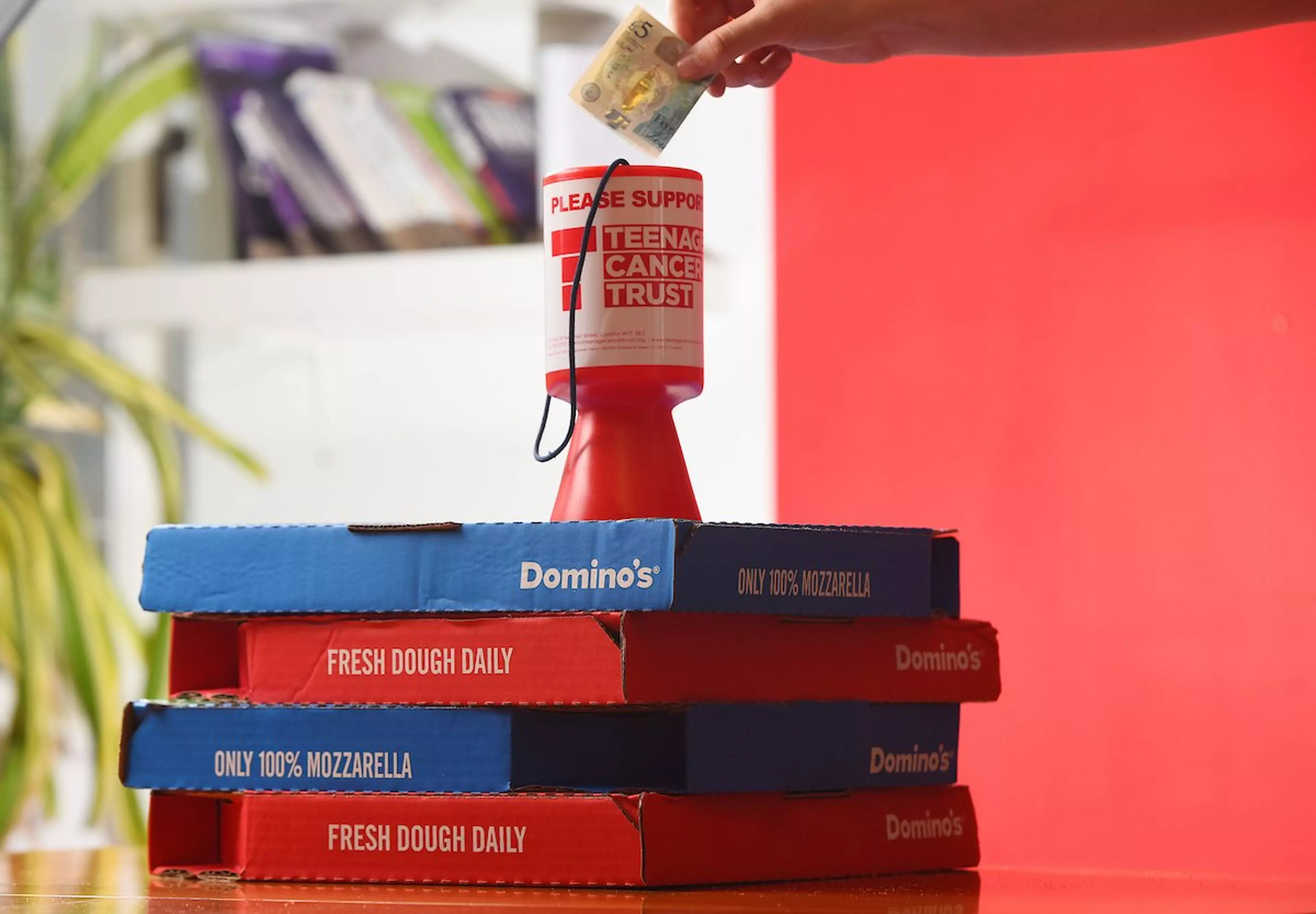 A person putting money into a teenage cancer trust donation box, sitting on a stack of pizza boxes