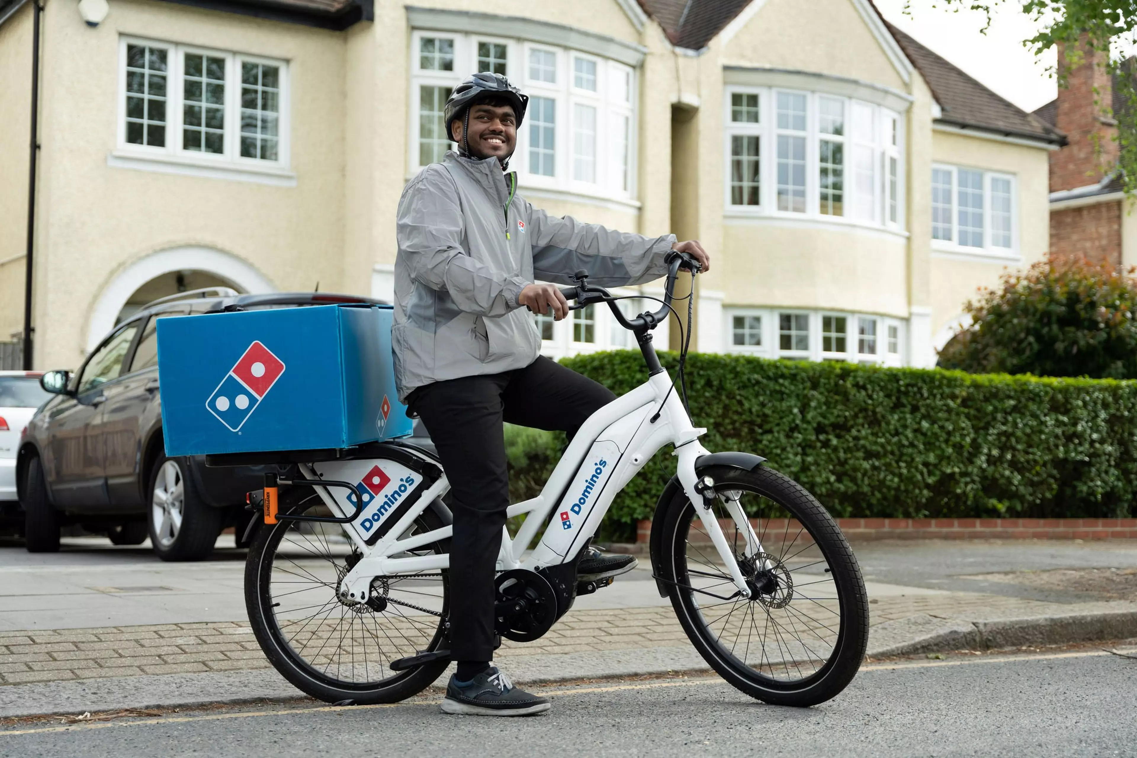 A Domino's delivery employee is sat on top of a bike outside.