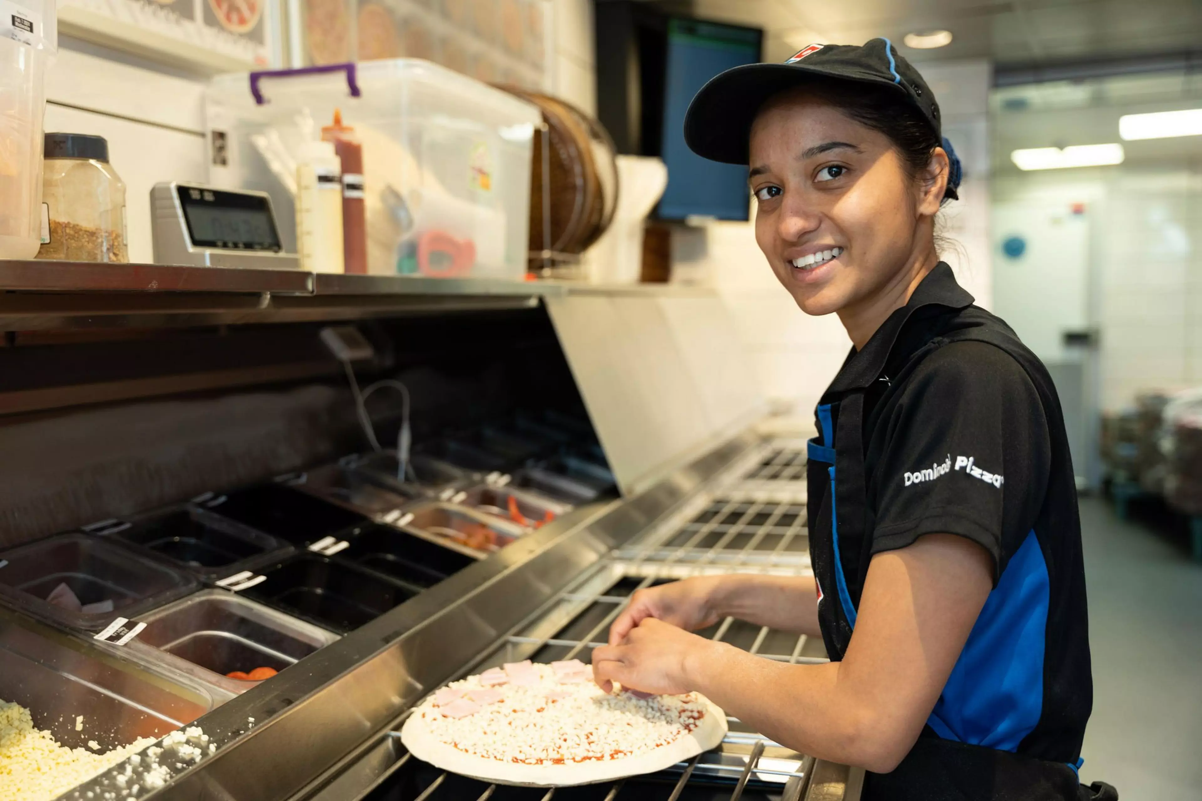 A woman in an Domino's uniform is in store preparing a pizza.