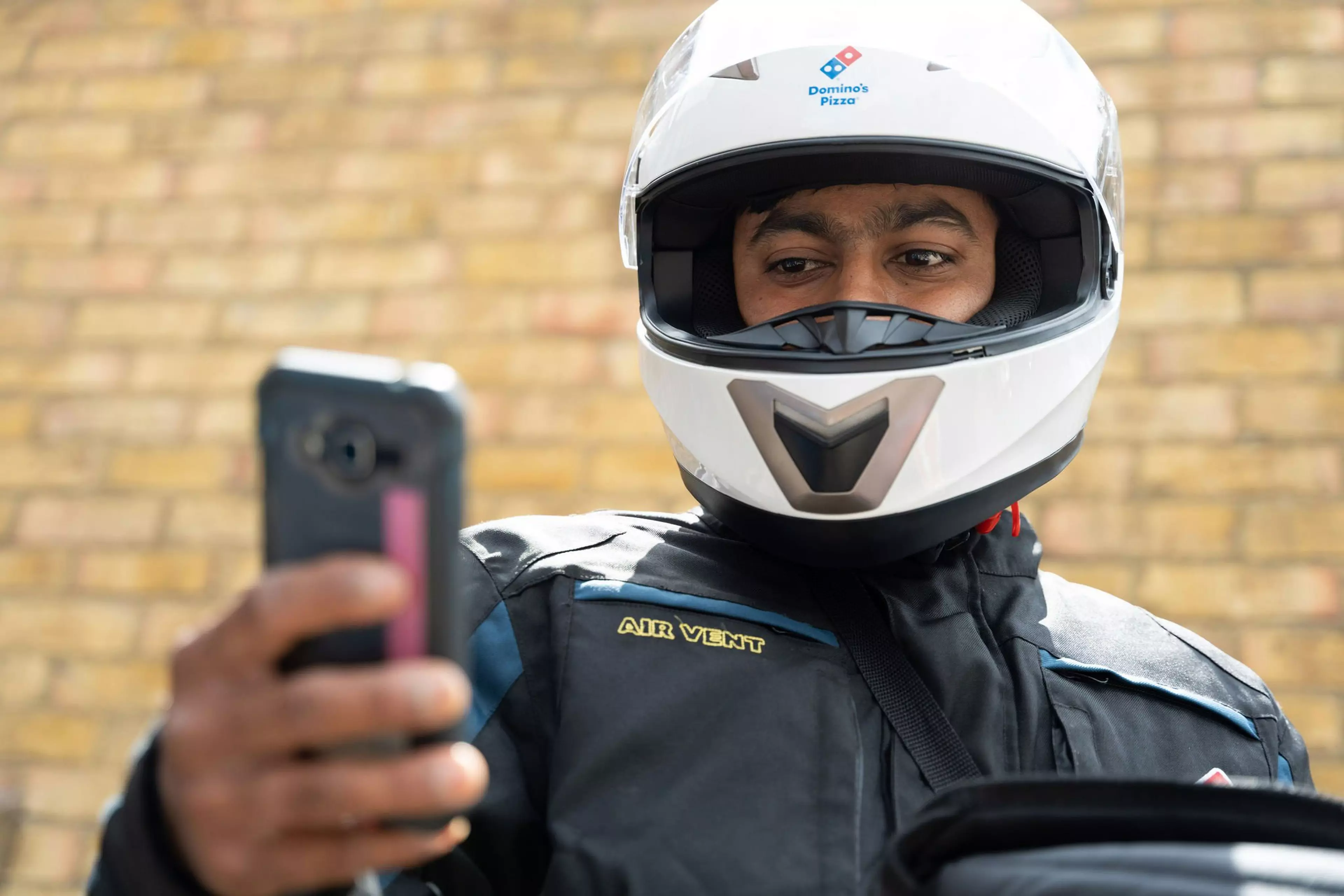 A Domino's delivery driver wearing a bike helmet is looking at his mobile phone.