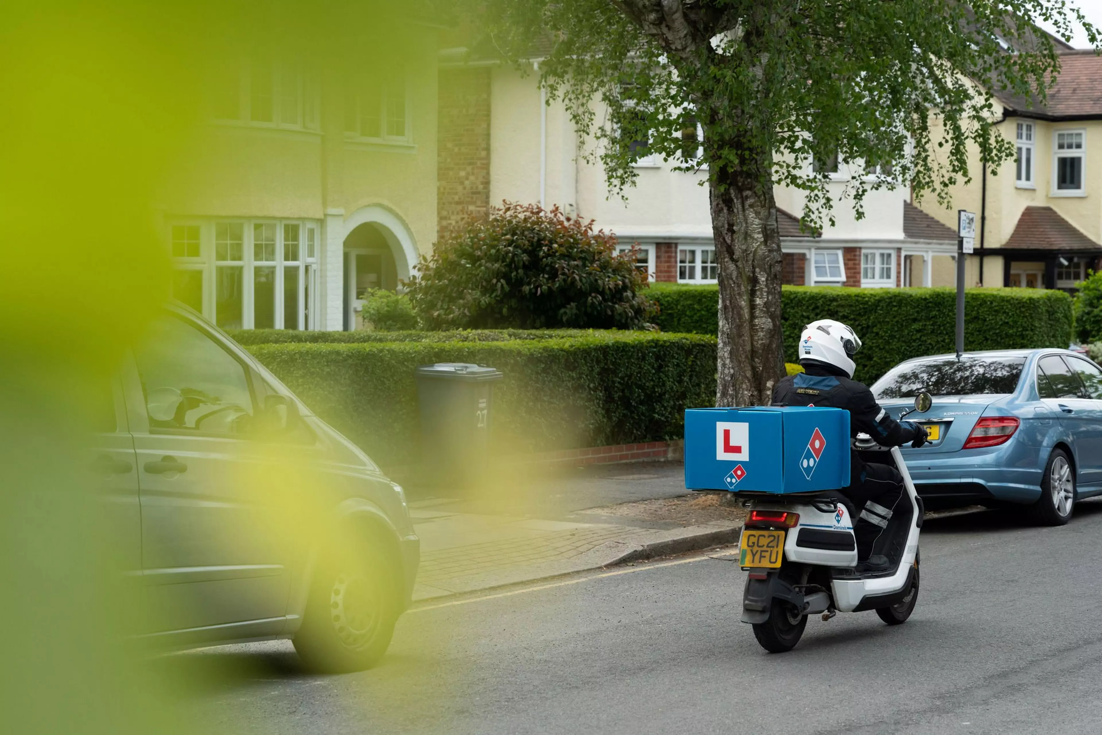 A Domino's delivery driver on a moped drives down a street.