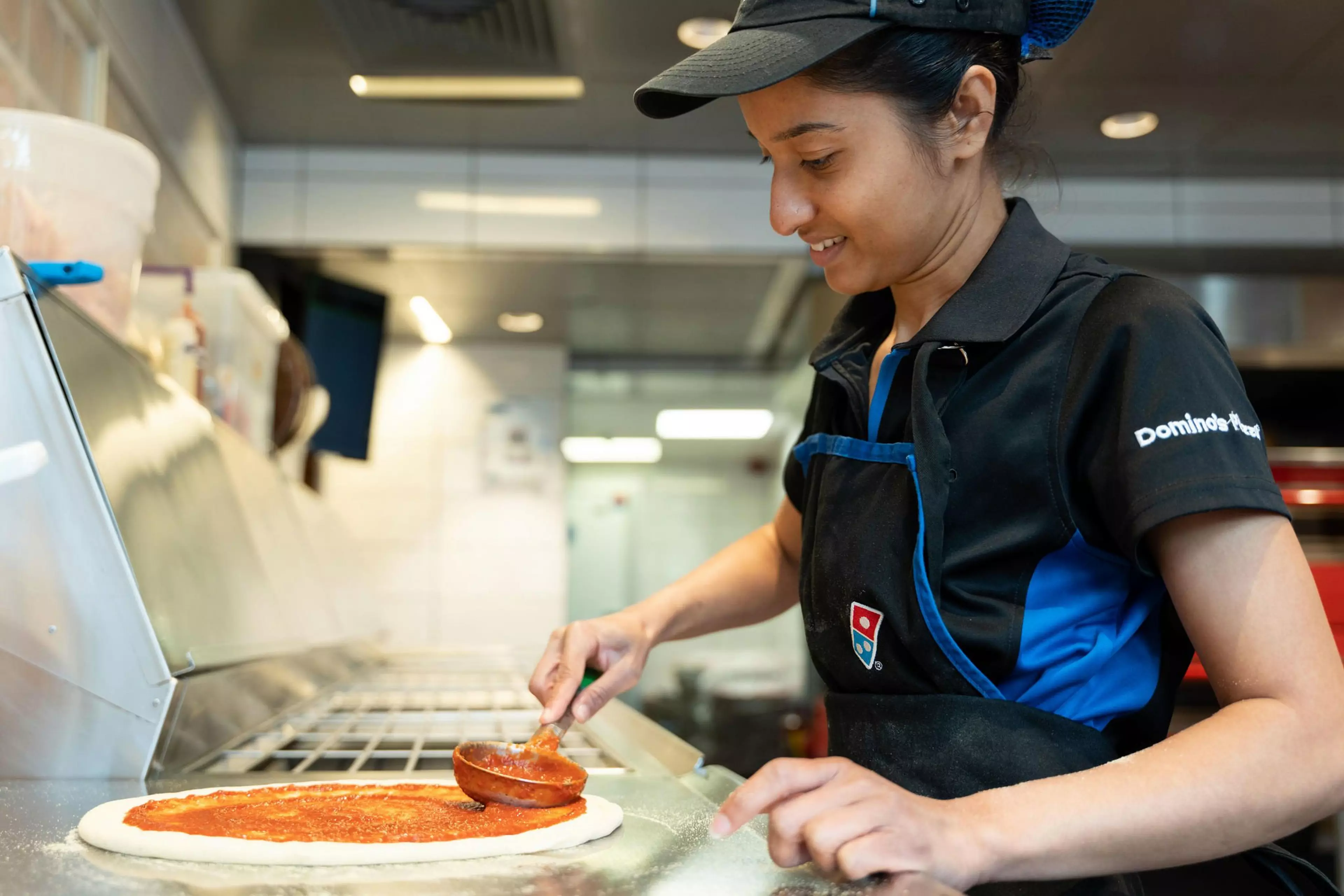 A picture of a Domino's worker in store spreading sauce onto a pizza base.