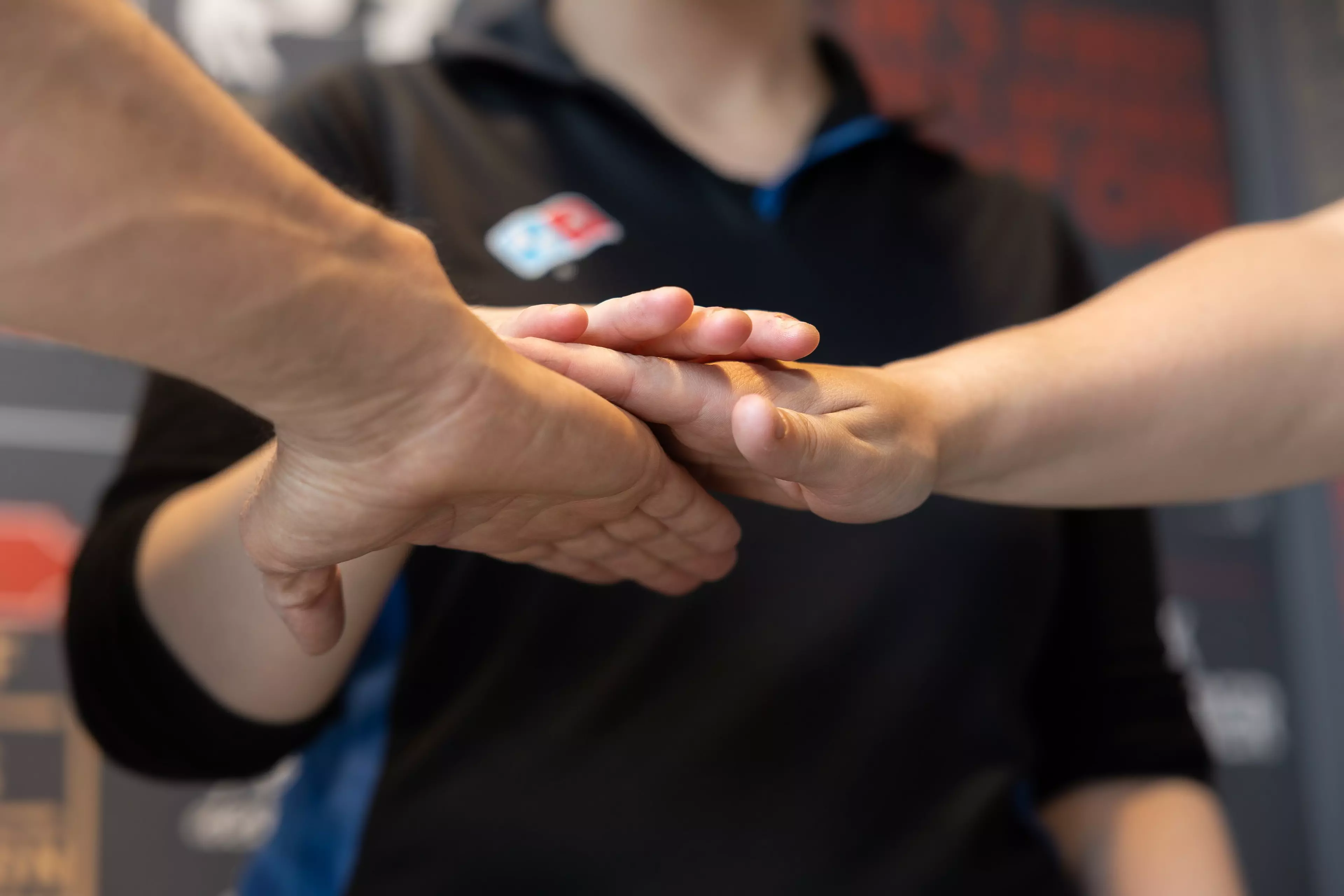 Close up of three people placing their hands together, two are out of view and one is wearing a Domino's uniform.